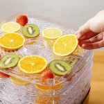 نحوه قرار دادن میوه‌هایی مانند پرتقال، کیوی و توت‌فرنگی بر روی سینی‌های شفاف دستگاه میوه خشک‌کن کولاکس