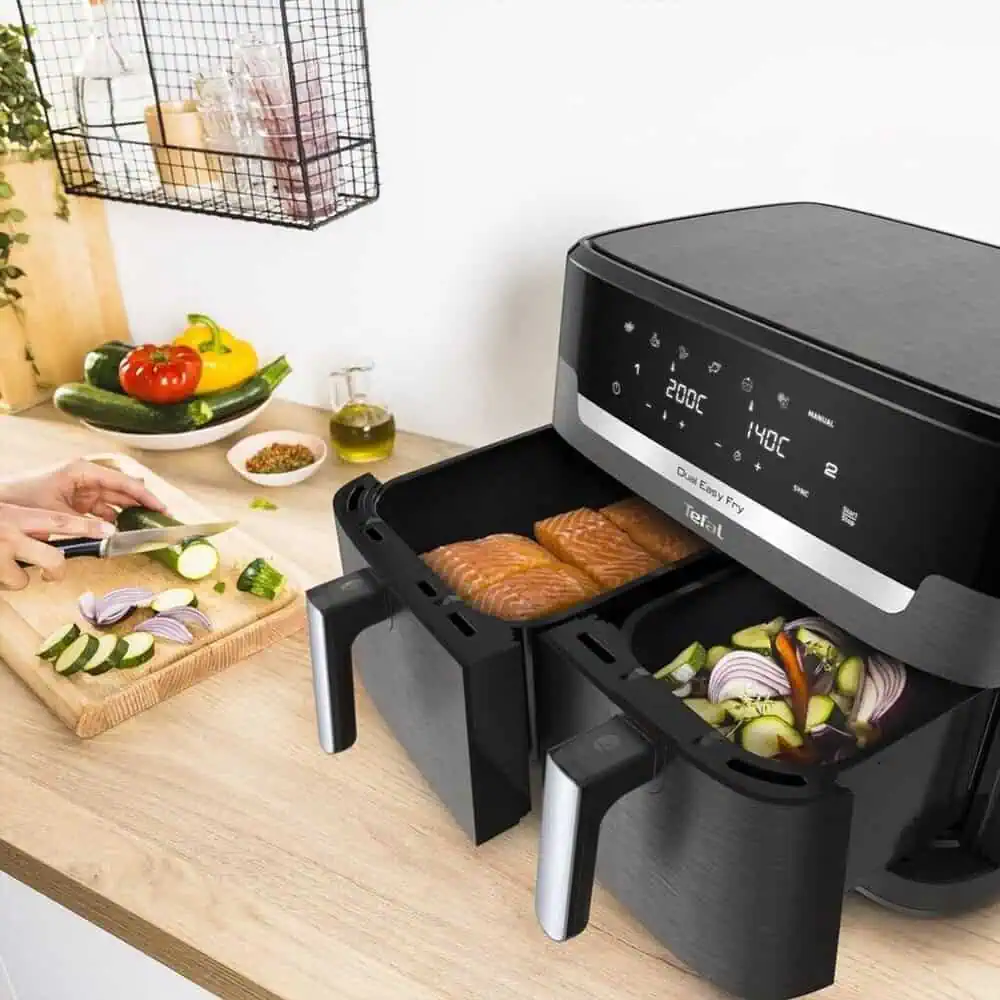 سرخکن دوقلو تفال Tefal EY942 در حال پخت ماهی سالمون و سبزیجات، روی میز آشپزخانه در کنار آمادهسازی مواد اولیه